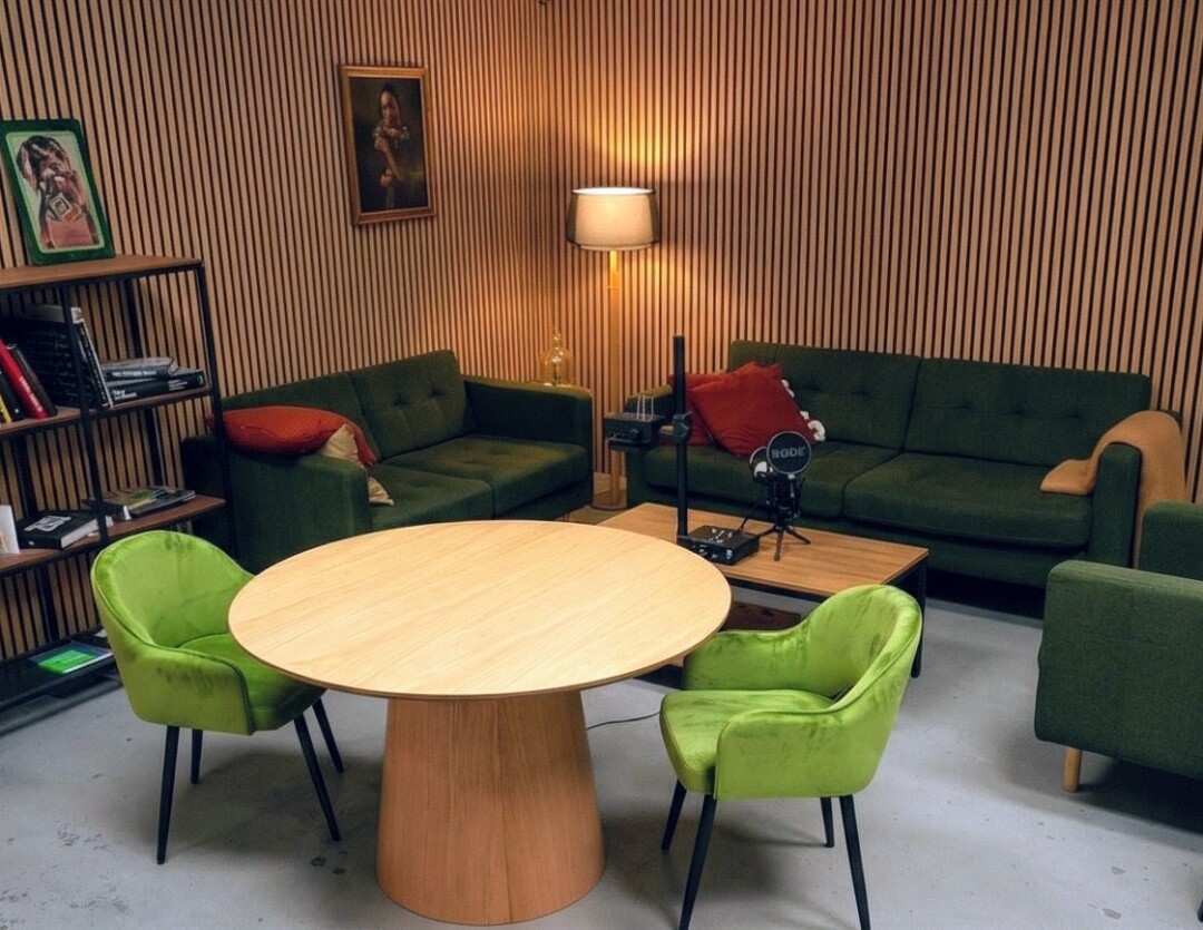 Vollständige Raumansicht des Podcast Studio Hannover mit Sprechertisch, Lounge-Bereich mit grünen Sofas und RØDE-Aufnahmetechnik.